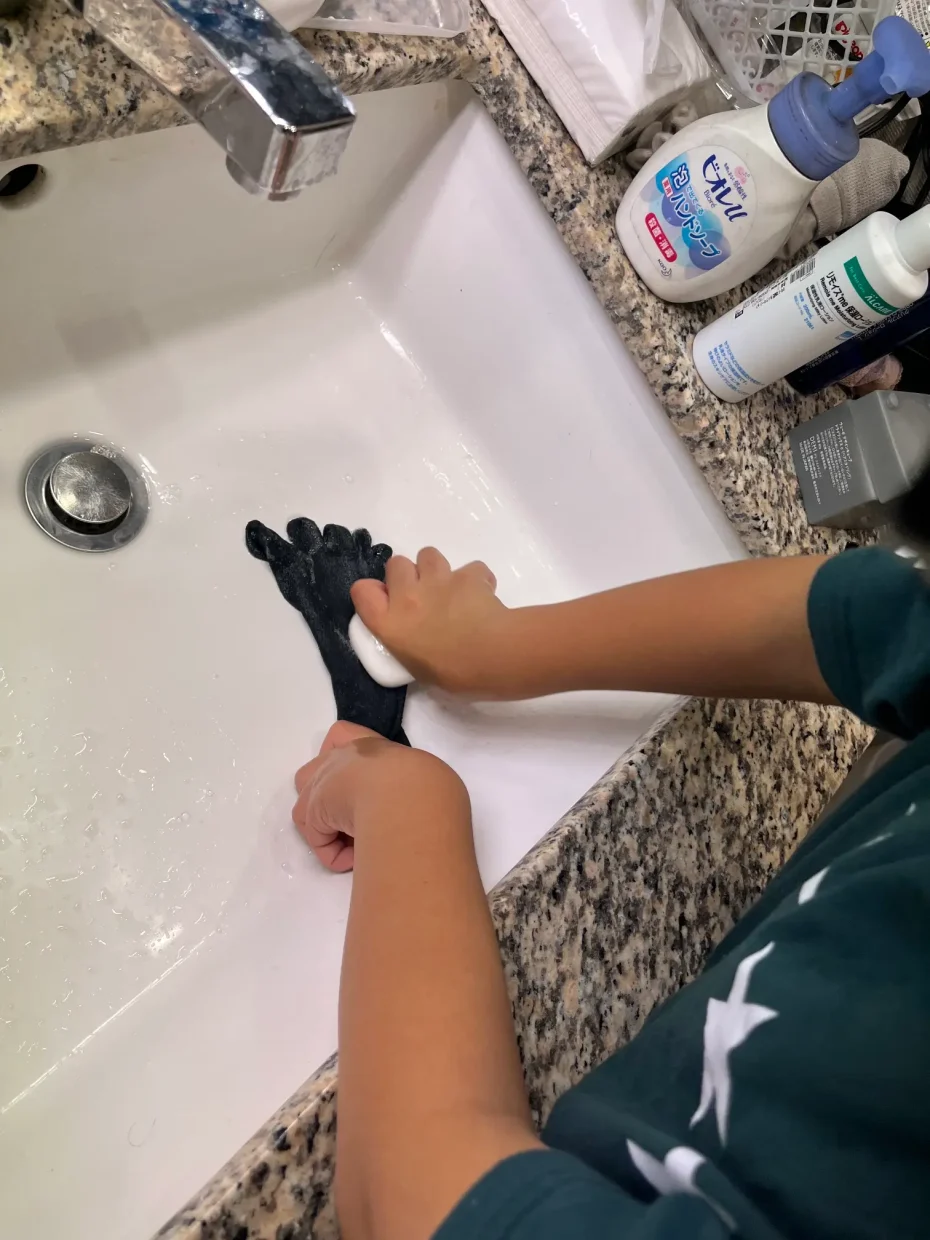 子どもが洗面ボウルで5本指ソックスのつま先に石けんをつけて予洗いしている手元