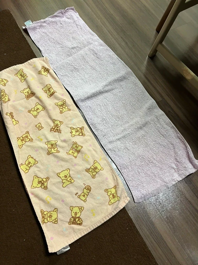 普通のフェイスタオルと紫のバスタオル卒業宣言を床に並べたサイズ比較