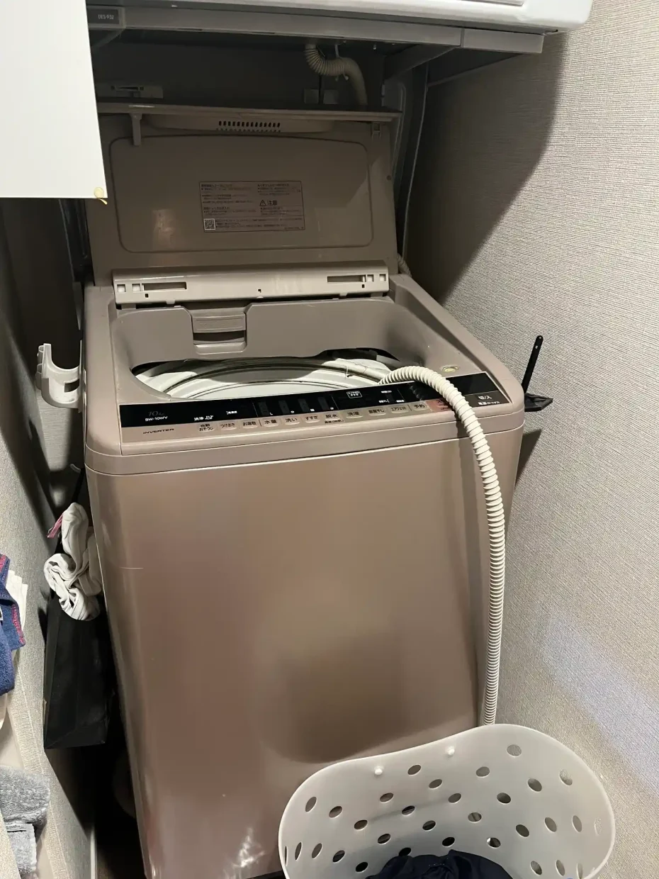 洗濯機横のホース掛けを使わず、お湯取ホースを空の洗濯槽へ入れている様子