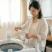 洗濯機の前で酸素系漂白剤とセスキプラスを準備する若いママ